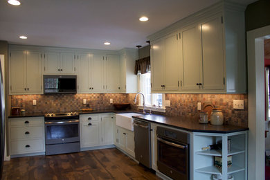 Eat-in kitchen - mid-sized craftsman l-shaped medium tone wood floor and brown floor eat-in kitchen idea in Bridgeport with a farmhouse sink, shaker cabinets, green cabinets, granite countertops, multicolored backsplash, slate backsplash, black appliances, no island and black countertops