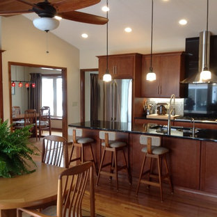 Design ideas for a large arts and crafts l-shaped eat-in kitchen in New York with a double-bowl sink, flat-panel cabinets, medium wood cabinets, granite benchtops, black splashback, glass tile splashback, stainless steel appliances, medium hardwood floors and with island.