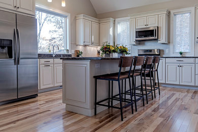 Large arts and crafts l-shaped light wood floor eat-in kitchen photo in Providence with an undermount sink, raised-panel cabinets, distressed cabinets, quartz countertops, beige backsplash, ceramic backsplash, stainless steel appliances and an island