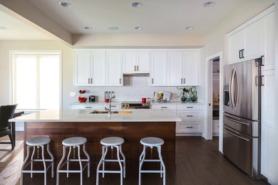 Inspiration for a mid-sized craftsman l-shaped dark wood floor and brown floor eat-in kitchen remodel in Other with a farmhouse sink, shaker cabinets, white cabinets, solid surface countertops, white backsplash, subway tile backsplash, stainless steel appliances and an island