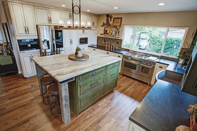 Example of a large arts and crafts u-shaped medium tone wood floor open concept kitchen design in Los Angeles with a farmhouse sink, raised-panel cabinets, distressed cabinets, granite countertops, brown backsplash, ceramic backsplash, stainless steel appliances and an island
