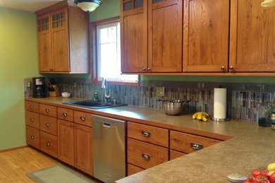 Example of a mid-sized arts and crafts medium tone wood floor eat-in kitchen design in Seattle with shaker cabinets, medium tone wood cabinets, laminate countertops, multicolored backsplash, glass tile backsplash, stainless steel appliances and a peninsula