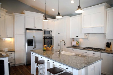 Example of a large arts and crafts u-shaped dark wood floor and brown floor open concept kitchen design in Other with a farmhouse sink, shaker cabinets, white cabinets, granite countertops, white backsplash, stainless steel appliances, an island and subway tile backsplash