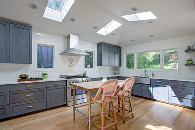 Example of an arts and crafts light wood floor eat-in kitchen design in San Francisco with a farmhouse sink, shaker cabinets, gray cabinets, quartz countertops, white backsplash, subway tile backsplash, stainless steel appliances and an island