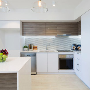 Contemporary l-shaped kitchen in Brisbane with a double-bowl sink, flat-panel cabinets, medium wood cabinets, white splashback, mosaic tile splashback, stainless steel appliances, light hardwood floors, with island, beige floor and white benchtop.