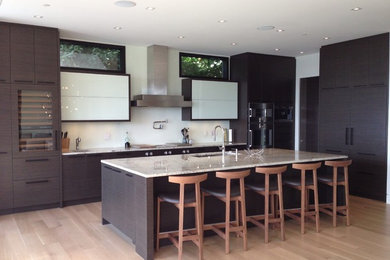 This is an example of a large contemporary l-shaped kitchen in Vancouver with a submerged sink, flat-panel cabinets, brown cabinets, granite worktops, white splashback, integrated appliances, light hardwood flooring, an island and brown floors.