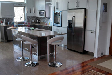 Photo of a medium sized contemporary l-shaped kitchen in Denver with a submerged sink, flat-panel cabinets, white cabinets, engineered stone countertops, multi-coloured splashback, matchstick tiled splashback, stainless steel appliances, porcelain flooring, an island and brown floors.