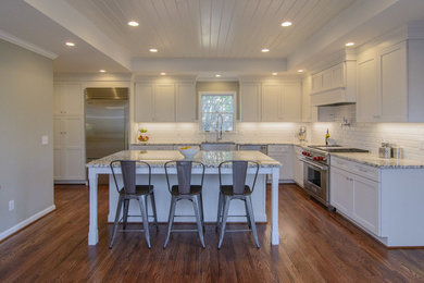 Example of a large country l-shaped dark wood floor eat-in kitchen design in Birmingham with a farmhouse sink, shaker cabinets, white cabinets, granite countertops, white backsplash, subway tile backsplash, stainless steel appliances and an island