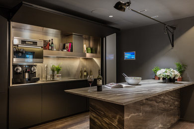 Photo of a small kitchen in Other with a submerged sink, flat-panel cabinets, black cabinets, granite worktops, metallic splashback, metal splashback, stainless steel appliances, an island and brown floors.