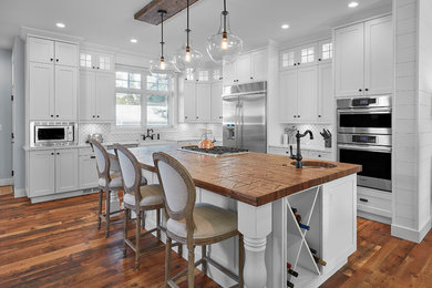 Example of a country l-shaped dark wood floor and brown floor kitchen design in Edmonton with shaker cabinets, white cabinets, white backsplash, stainless steel appliances and an island