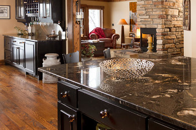 Cette image montre une cuisine américaine encastrable chalet avec un placard à porte vitrée, des portes de placard noires, un plan de travail en granite, une crédence métallisée et un sol en bois brun.