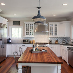 This is an example of a mid-sized traditional u-shaped separate kitchen in Philadelphia with a farmhouse sink, glass-front cabinets, white cabinets, concrete benchtops, white splashback, subway tile splashback, stainless steel appliances, bamboo floors and with island.