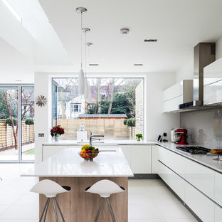 Modelo de cocina actual con fregadero bajoencimera, armarios con paneles lisos, puertas de armario blancas, salpicadero verde, salpicadero de vidrio templado, electrodomésticos de acero inoxidable y una isla