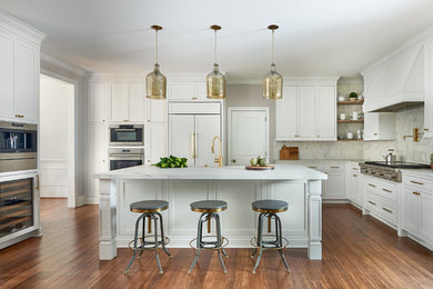 Example of a transitional l-shaped medium tone wood floor enclosed kitchen design in Charlotte with shaker cabinets, white cabinets, white backsplash, paneled appliances, an island and white countertops