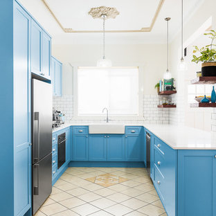 Inspiration for a mid-sized transitional u-shaped kitchen in Sydney with a farmhouse sink, blue cabinets, white splashback, subway tile splashback, stainless steel appliances, beige floor, shaker cabinets, solid surface benchtops, terra-cotta floors, with island and white benchtop.