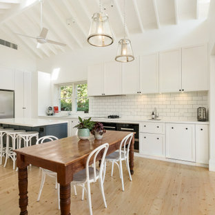 Transitional l-shaped eat-in kitchen in Sydney with an undermount sink, shaker cabinets, white cabinets, white splashback, subway tile splashback, black appliances, light hardwood floors, with island, beige floor, white benchtop, exposed beam and vaulted.