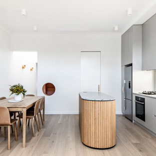 Contemporary galley eat-in kitchen in Sydney with a double-bowl sink, flat-panel cabinets, grey cabinets, quartz benchtops, window splashback, stainless steel appliances, medium hardwood floors, with island, brown floor and white benchtop.