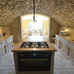 Inspiration for a country kitchen in Florence with an integrated sink, recessed-panel cabinets, distressed cabinets, wood benchtops, travertine splashback, black appliances, limestone floors and with island.