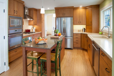 Foto på ett mellanstort funkis kök, med en nedsänkt diskho, släta luckor, skåp i mellenmörkt trä, laminatbänkskiva, beige stänkskydd, rostfria vitvaror, bambugolv och en köksö