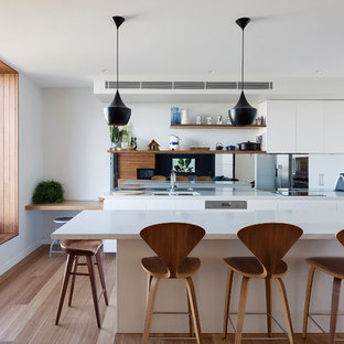 Design ideas for a contemporary l-shaped eat-in kitchen in Sydney with an undermount sink, flat-panel cabinets, white cabinets, mirror splashback, stainless steel appliances, medium hardwood floors, with island, brown floor and white benchtop.