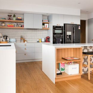 Photo of a midcentury l-shaped kitchen in Canberra - Queanbeyan with an undermount sink, flat-panel cabinets, grey cabinets, white splashback, mosaic tile splashback, medium hardwood floors, with island, brown floor and white benchtop.