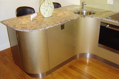 Foto på ett mellanstort funkis kök, med en enkel diskho, luckor med glaspanel, granitbänkskiva, rostfria vitvaror, bambugolv, skåp i rostfritt stål, stänkskydd med metallisk yta och glaspanel som stänkskydd
