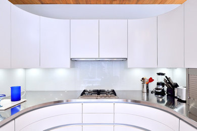 ワシントンD.C.にあるラグジュアリーな小さなコンテンポラリースタイルのおしゃれなキッチン (一体型シンク、フラットパネル扉のキャビネット、白いキャビネット、ステンレスカウンター、ガラス板のキッチンパネル、シルバーの調理設備) の写真