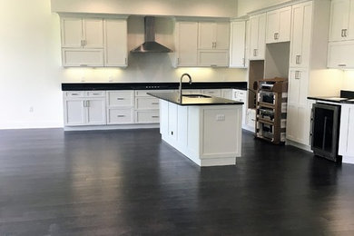 Mittelgroße Moderne Küche in L-Form mit Schrankfronten im Shaker-Stil, weißen Schränken, Quarzit-Arbeitsplatte, Küchengeräten aus Edelstahl, dunklem Holzboden, Kücheninsel, braunem Boden und Unterbauwaschbecken in Tampa