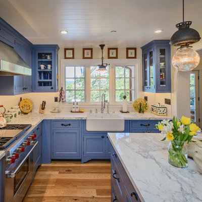 Example of a mid-sized country l-shaped medium tone wood floor and brown floor open concept kitchen design in San Francisco with a farmhouse sink, blue cabinets, marble countertops, white backsplash, subway tile backsplash, stainless steel appliances, an island and shaker cabinets