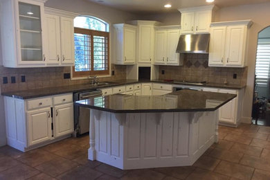 Mid-sized transitional l-shaped terra-cotta tile enclosed kitchen photo in Orange County with a double-bowl sink, raised-panel cabinets, white cabinets, solid surface countertops, beige backsplash, stone tile backsplash, stainless steel appliances and an island