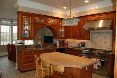 Example of a mid-sized classic l-shaped ceramic tile eat-in kitchen design in Houston with a drop-in sink, glass-front cabinets, medium tone wood cabinets, wood countertops, beige backsplash, ceramic backsplash, stainless steel appliances and an island