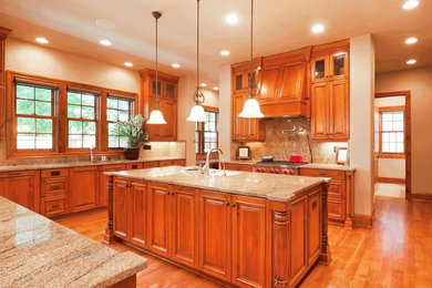 Large elegant u-shaped light wood floor open concept kitchen photo in Philadelphia with a drop-in sink, raised-panel cabinets, medium tone wood cabinets, granite countertops, brown backsplash, stone slab backsplash, stainless steel appliances and an island