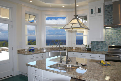 Example of a large beach style concrete floor and turquoise floor kitchen design in San Diego with a farmhouse sink, raised-panel cabinets, white cabinets, granite countertops, blue backsplash, glass tile backsplash, stainless steel appliances, two islands and multicolored countertops