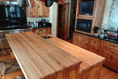 Eat-in kitchen - large rustic l-shaped medium tone wood floor eat-in kitchen idea in Denver with an undermount sink, raised-panel cabinets, medium tone wood cabinets, wood countertops, stainless steel appliances and an island