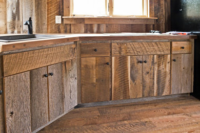 Idées déco pour une cuisine montagne en bois vieilli de taille moyenne avec un évier posé, un placard à porte plane, un plan de travail en bois, une crédence marron, une crédence en bois, un électroménager noir et un sol en bois brun.
