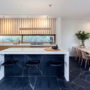 This is an example of a midcentury galley eat-in kitchen in Melbourne with an undermount sink, flat-panel cabinets, light wood cabinets, window splashback, stainless steel appliances, with island, black floor and white benchtop.