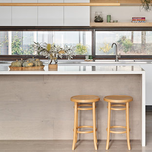 Photo of a large contemporary galley kitchen in Melbourne with flat-panel cabinets, white cabinets, window splashback, medium hardwood floors, with island, brown floor and white benchtop.
