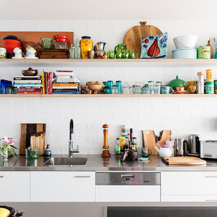 Photo of a modern galley kitchen in Sydney with an integrated sink, flat-panel cabinets, white cabinets, stainless steel benchtops, white splashback, subway tile splashback, with island and grey benchtop.