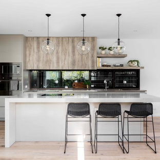 Mid-sized modern galley eat-in kitchen in Sydney with an integrated sink, flat-panel cabinets, window splashback, black appliances, light hardwood floors, with island and white benchtop.