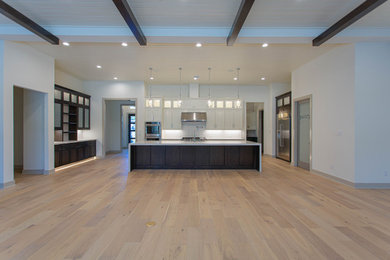 Example of a large minimalist u-shaped light wood floor, beige floor and exposed beam eat-in kitchen design in Houston with an undermount sink, shaker cabinets, white cabinets, marble countertops, white backsplash, subway tile backsplash, stainless steel appliances, an island and white countertops