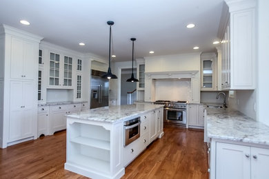 Inspiration for a large timeless u-shaped medium tone wood floor eat-in kitchen remodel in Philadelphia with an undermount sink, glass-front cabinets, white cabinets, marble countertops, white backsplash, wood backsplash, stainless steel appliances and an island