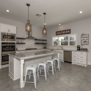 Mid-sized farmhouse open concept kitchen ideas - Example of a mid-sized farmhouse u-shaped concrete floor and gray floor open concept kitchen design in Austin with a farmhouse sink, shaker cabinets, white cabinets, granite countertops, white backsplash, subway tile backsplash, stainless steel appliances and an island
