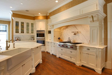 Inspiration for a farmhouse medium tone wood floor kitchen remodel in Bridgeport with a farmhouse sink, recessed-panel cabinets, white cabinets, marble countertops, gray backsplash, stone slab backsplash, stainless steel appliances and an island