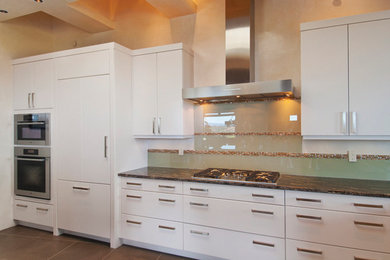 This is an example of a medium sized contemporary kitchen in Albuquerque with flat-panel cabinets, white cabinets, granite worktops, green splashback, glass sheet splashback, stainless steel appliances and brown floors.