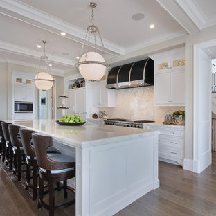Foto di una grande cucina stile marinaro con lavello stile country, ante con riquadro incassato, ante bianche, top in marmo, paraspruzzi bianco, paraspruzzi in lastra di pietra, elettrodomestici in acciaio inossidabile, pavimento in legno massello medio, isola e pavimento marrone