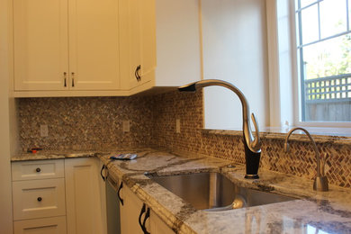 Example of a mid-sized trendy u-shaped eat-in kitchen design in Vancouver with a double-bowl sink, recessed-panel cabinets, white cabinets, granite countertops, multicolored backsplash, glass tile backsplash and stainless steel appliances