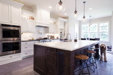 Inspiration for a transitional medium tone wood floor and brown floor eat-in kitchen remodel in Portland with a farmhouse sink, shaker cabinets, white cabinets, white backsplash, subway tile backsplash, stainless steel appliances, an island and white countertops