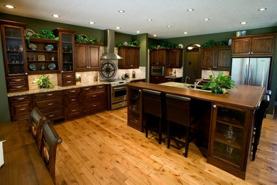 Exemple d'une grande cuisine américaine nature en L et bois foncé avec un évier encastré, un placard avec porte à panneau surélevé, un électroménager en acier inoxydable, un sol en bois brun et îlot.