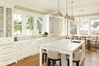 Large transitional galley medium tone wood floor and brown floor open concept kitchen photo in Charleston with a farmhouse sink, white cabinets, marble countertops, flat-panel cabinets, gray backsplash, subway tile backsplash, stainless steel appliances and an island