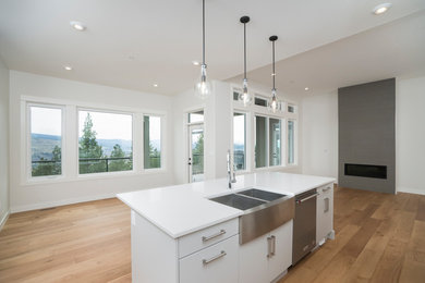 Example of a mid-sized minimalist l-shaped light wood floor and brown floor open concept kitchen design in Calgary with a farmhouse sink, flat-panel cabinets, white cabinets, solid surface countertops, stainless steel appliances, an island and white countertops
